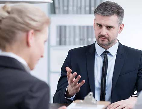 A man interviews a woman during a vet compliance assessment in an office setting.