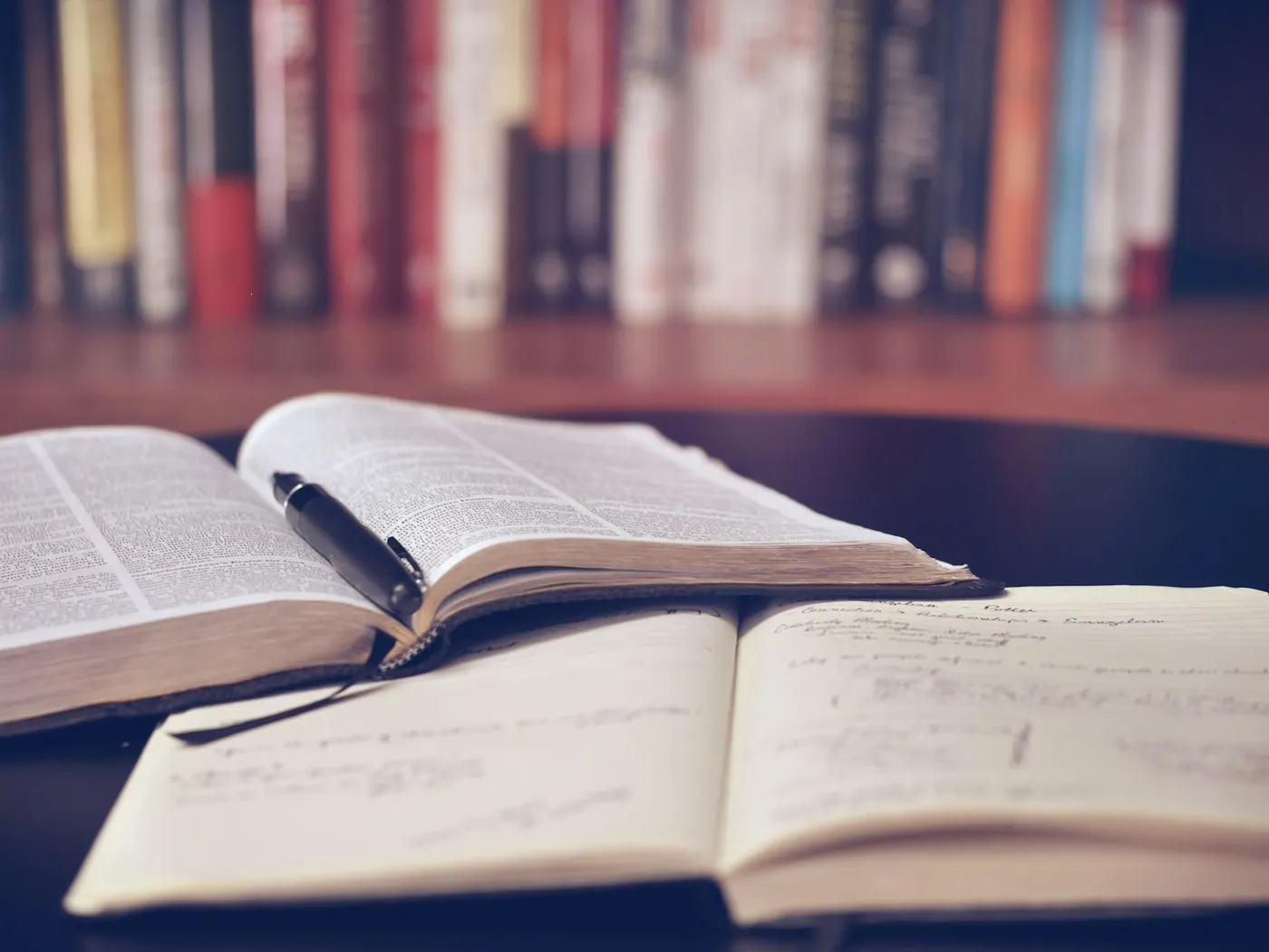 Open books and a pen rest on a table with bookshelves, representing vocational education training resources.