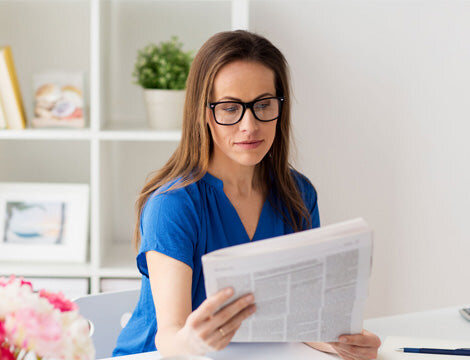 A woman wearing glasses reads a newspaper, staying informed about vocational education and training.