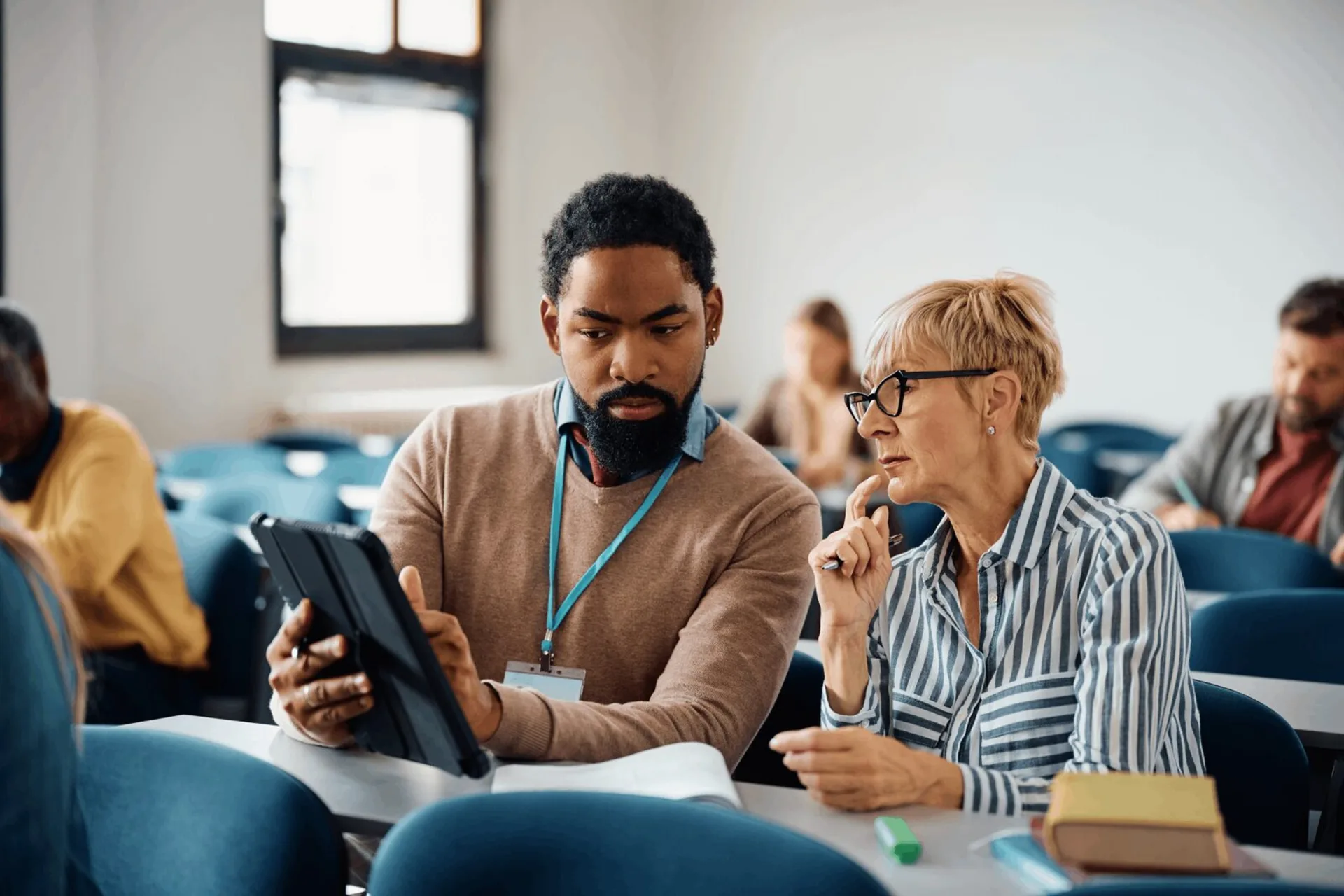 A man and woman collaborate on a tablet during an adult education training session.